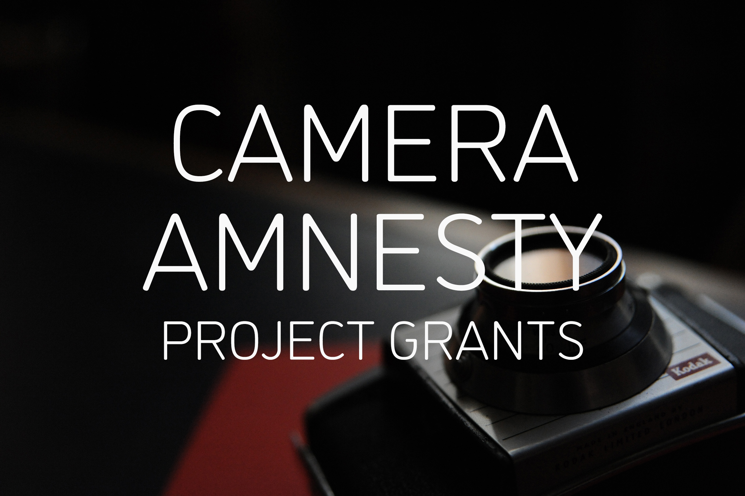 Graphic with an image of a film camera on a red notebook in the background and text reading 'CAMERA AMNESTY PROJECT GRANTS' in white in the centre.