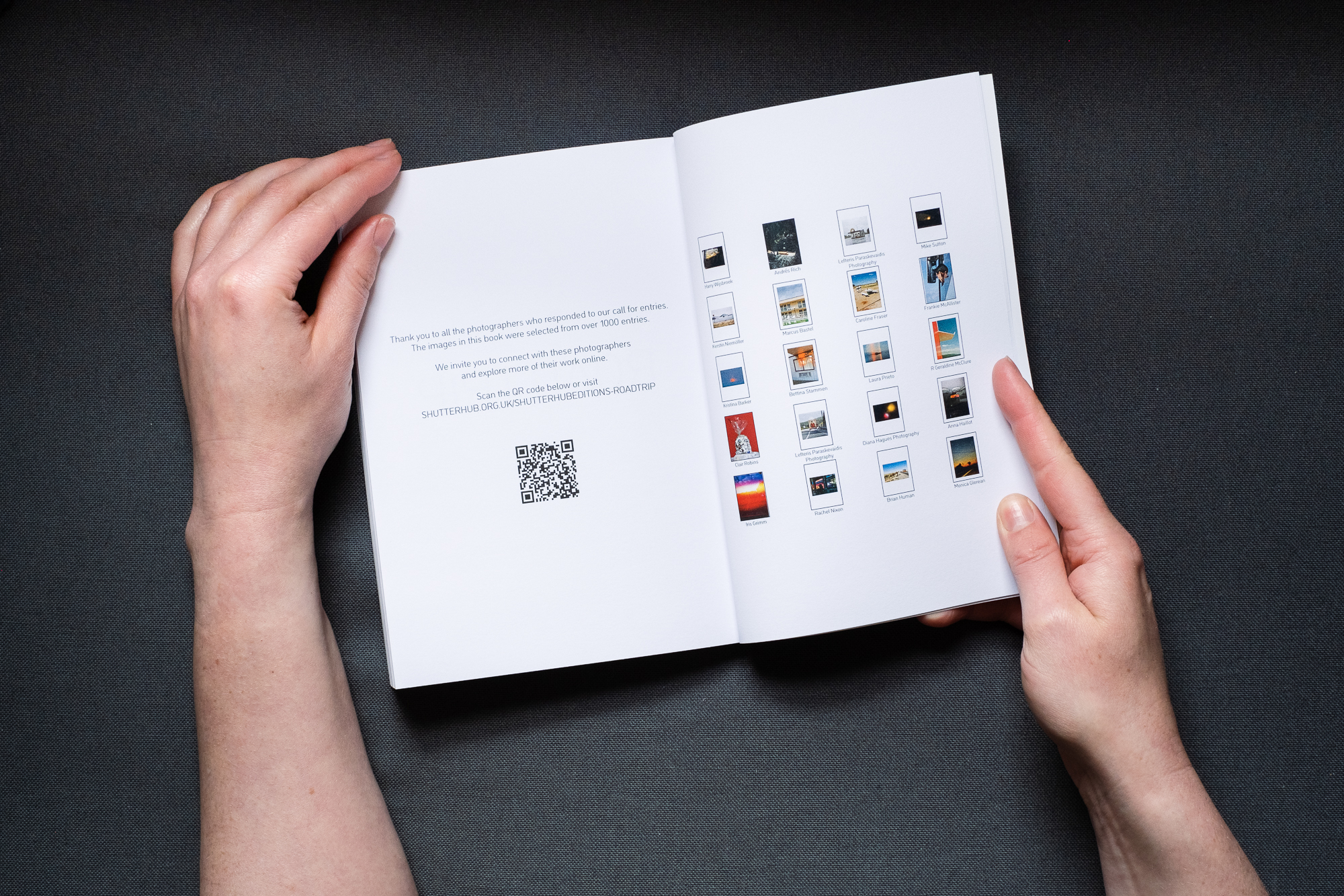 Photograph of the ROAD TRIP printed publication being held open by hands, on a dark grey background. The left page shows some text and a QR code and the right page shows thumbnails of images from the book with the photographers' names beneath.